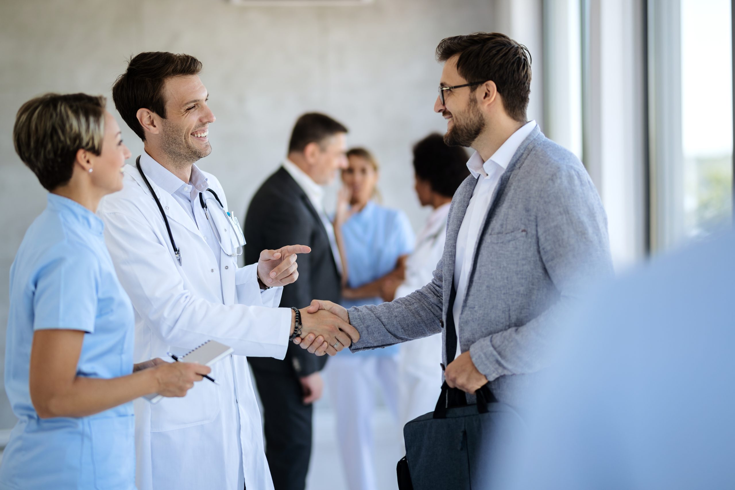 Happy doctor shaking hands with a businessman while greeting in a hallway at medical clinic.